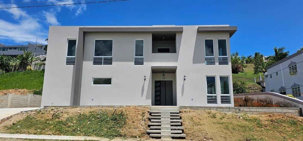 A modern two-story house with a gray exterior, large windows, and concrete front steps — D-26 MANSIONES PLAYA HUCARES, NAGUABO, PR