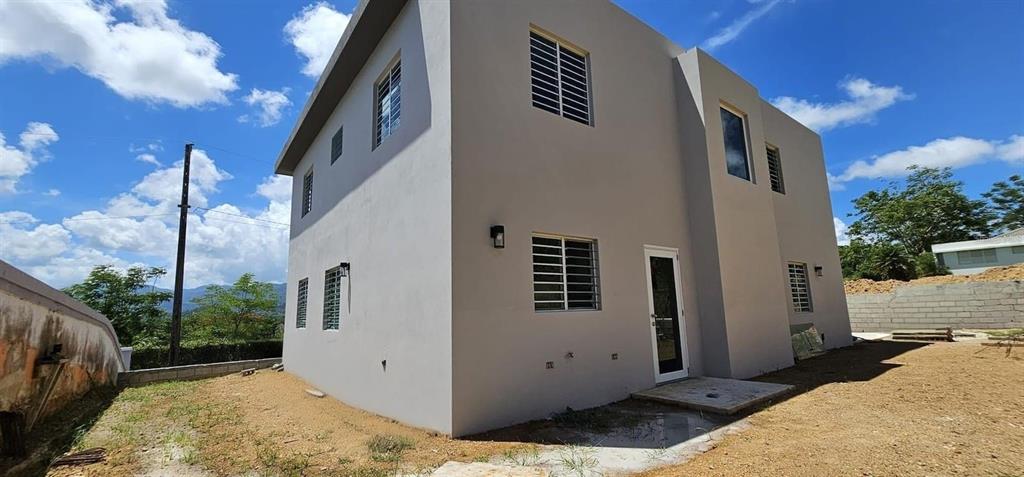 A two-story, light-colored concrete house with a glass door and metal window security bars — D-26 MANSIONES PLAYA HUCARES, NAGUABO, PR