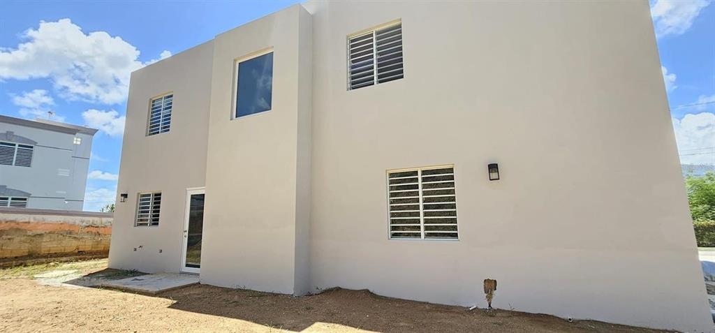 The exterior of a two-story beige house features multiple windows with white security bars — D-26 MANSIONES PLAYA HUCARES, NAGUABO, PR