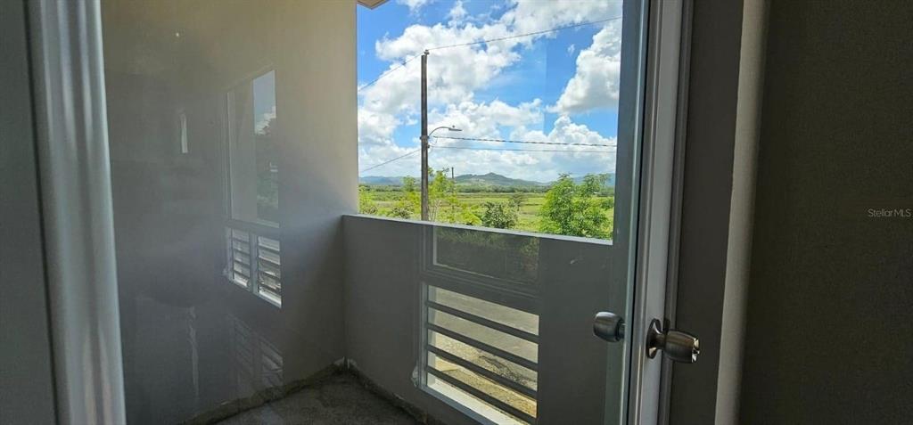 A view from an indoor balcony looking out toward a rural landscape and distant mountains — D-26 MANSIONES PLAYA HUCARES, NAGUABO, PR