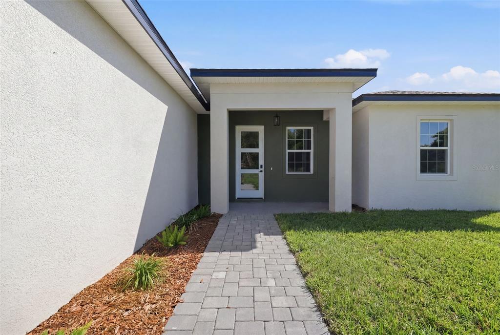 A paved walkway leads to the front entrance of a house with white stucco walls — 16835 SW 17TH TERRACE, OCALA, FL