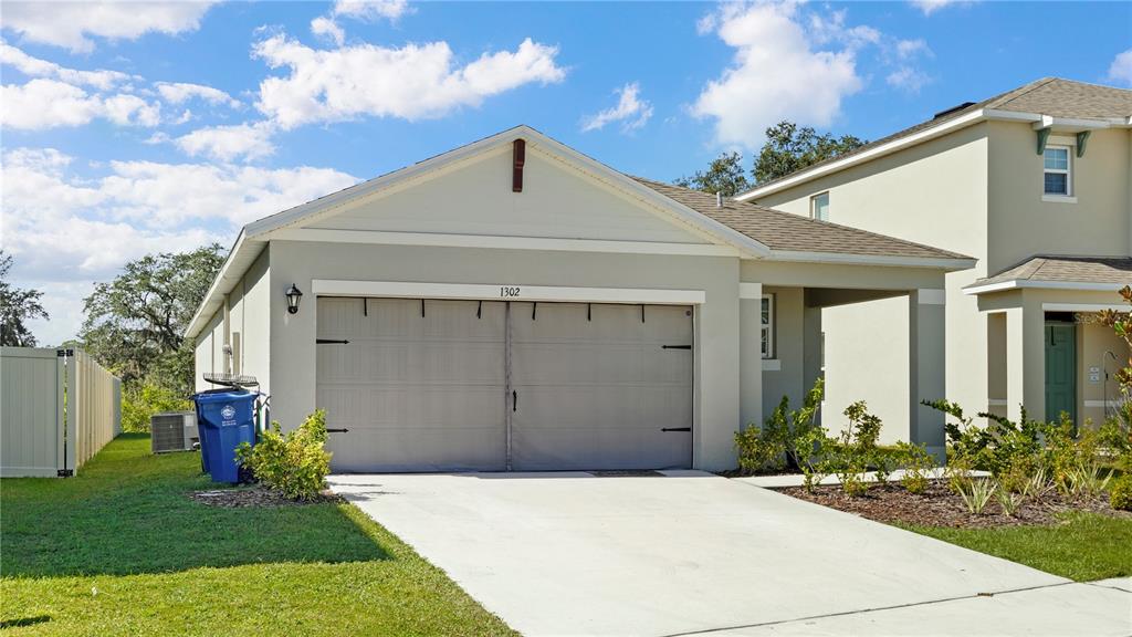 A single-story house with a two-car garage and a concrete driveway under a blue sky — 1302 HOLODAK DRIVE, DAVENPORT, FL