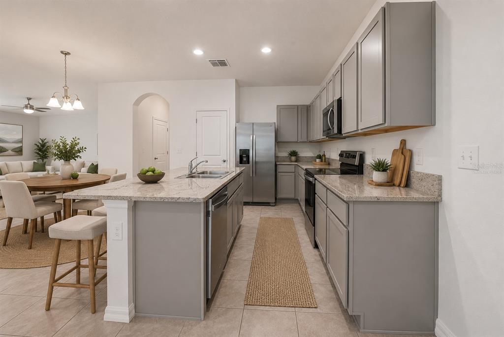 A modern kitchen features gray cabinets, granite countertops, a central island, and stainless steel appliances — 1574 HUBBELL ROAD, WESLEY CHAPEL, FL