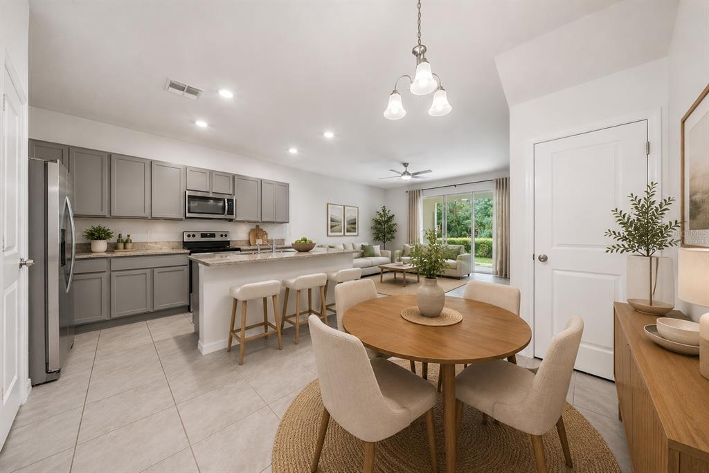 An open-concept kitchen and dining area features gray cabinets, a breakfast bar, and tile flooring — 1574 HUBBELL ROAD, WESLEY CHAPEL, FL