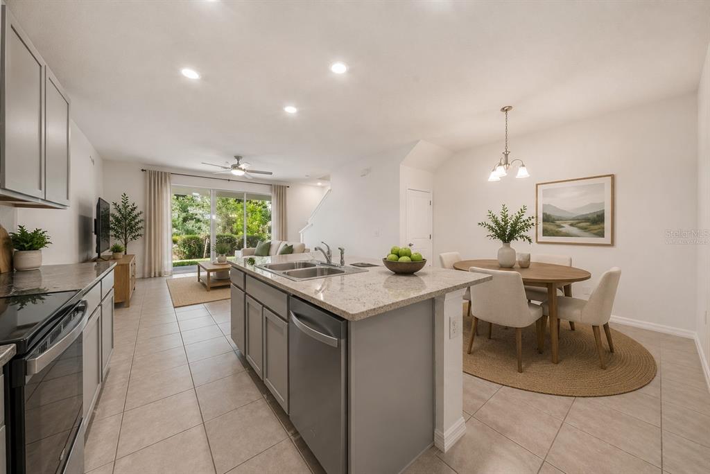 A kitchen with gray cabinets and a granite island opens to a dining area — 1574 HUBBELL ROAD, WESLEY CHAPEL, FL