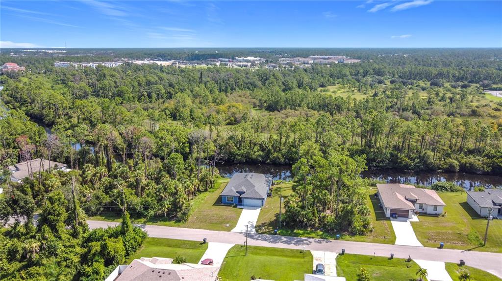 An aerial view shows suburban houses along a street bordering a dense wooded area — 2144 SADNET LANE, NORTH PORT, FL