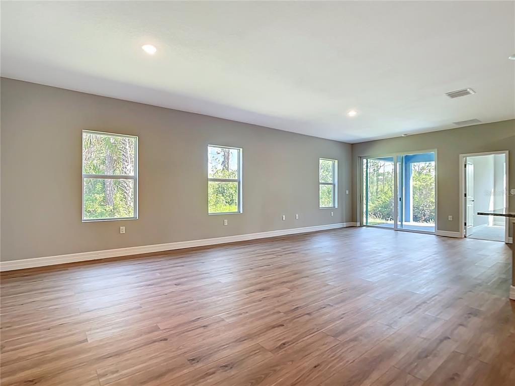 A spacious, empty living room features light gray walls, wood-look flooring, and sliding glass doors — 2144 SADNET LANE, NORTH PORT, FL