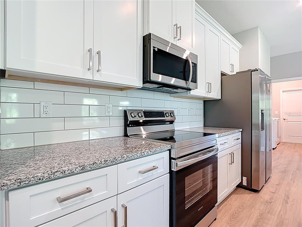 A kitchen features white cabinets, granite countertops, stainless steel appliances, and a white subway tile backsplash — 2144 SADNET LANE, NORTH PORT, FL