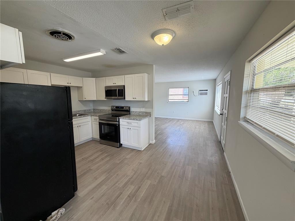 A kitchen with white cabinets and stainless steel appliances opens into a living area — 2007 9TH STREET NE, WINTER HAVEN, FL