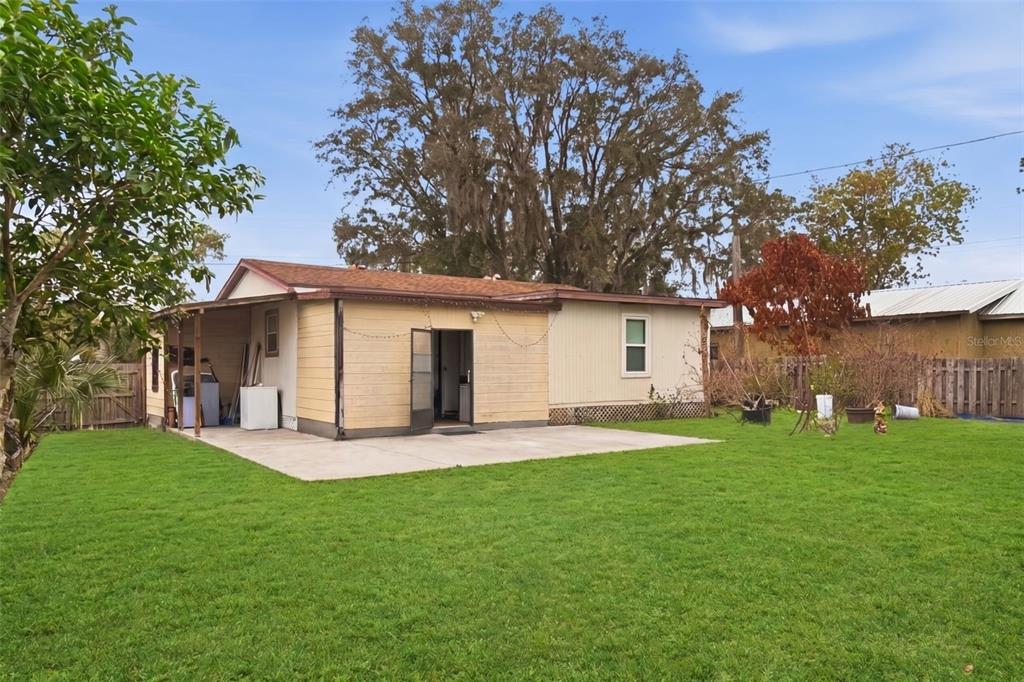 A backyard view of a single-story house with a concrete patio and a covered porch — 5521 SHARON AVENUE, INTERCESSION CITY, FL