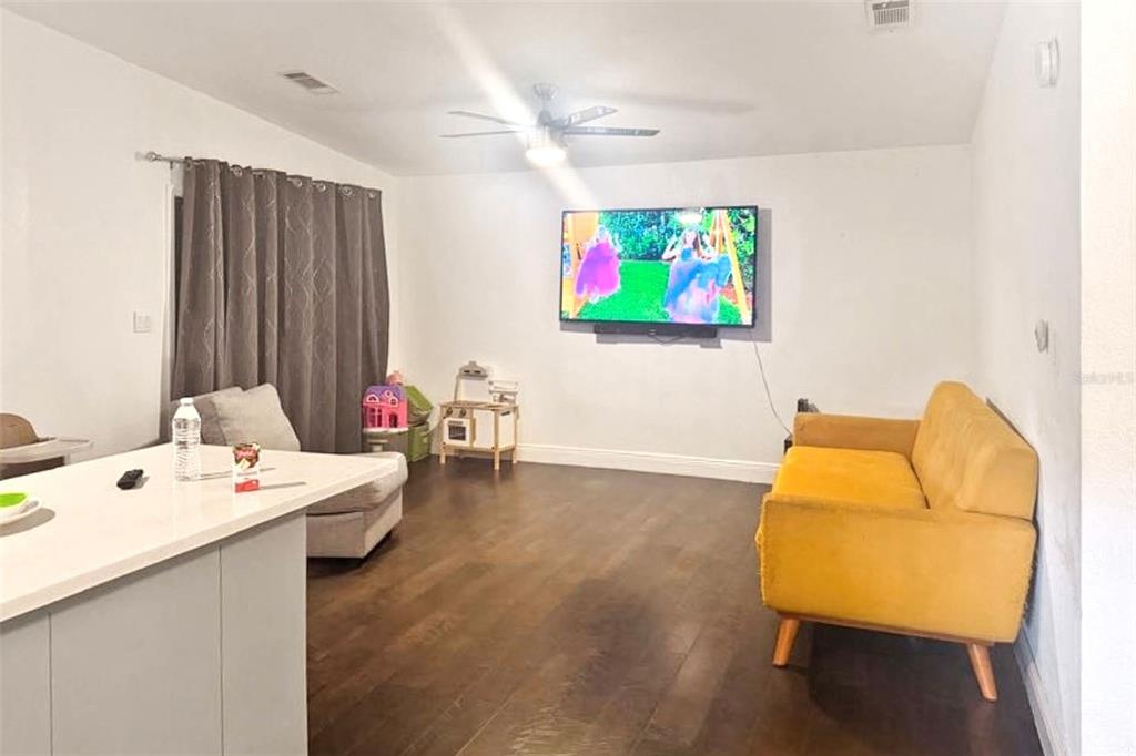 A living room features dark wood flooring, a yellow sofa, and a wall-mounted television — 5521 SHARON AVENUE, INTERCESSION CITY, FL