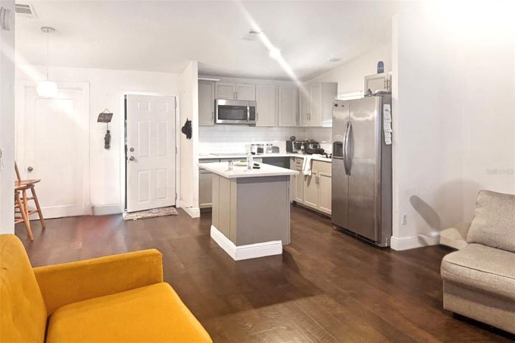 A kitchen with gray cabinets, stainless steel appliances, and an island opens into a living area — 5521 SHARON AVENUE, INTERCESSION CITY, FL