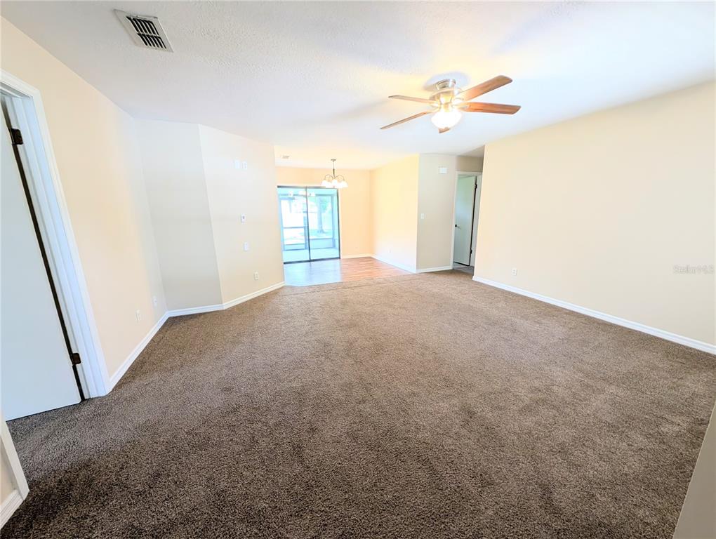 A spacious living room features beige walls, brown carpeting, a ceiling fan, and sliding doors — 3243 NE 32ND AVENUE, OCALA, FL