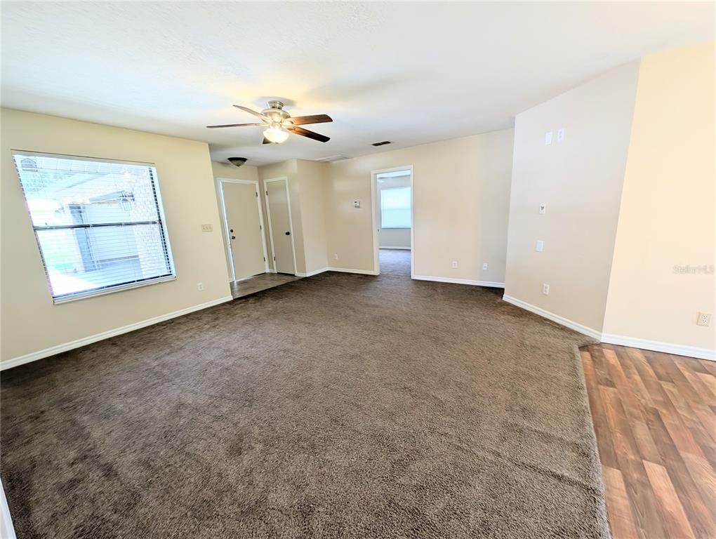 A living room with brown wall-to-wall carpeting, beige walls, a ceiling fan, and a window — 3243 NE 32ND AVENUE, OCALA, FL