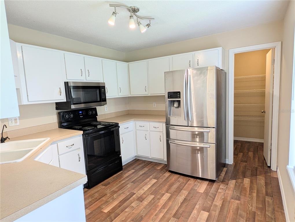 A kitchen features white cabinets, stainless steel appliances, tan countertops, and wood-look flooring — 3243 NE 32ND AVENUE, OCALA, FL