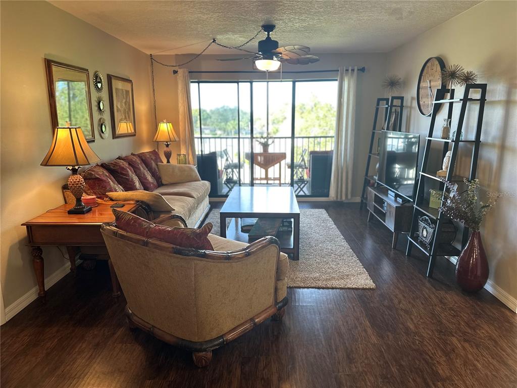 A living room features dark wood flooring, a ceiling fan, and a sliding glass door — 6116 43RD STREET W UNIT 401D, BRADENTON, FL