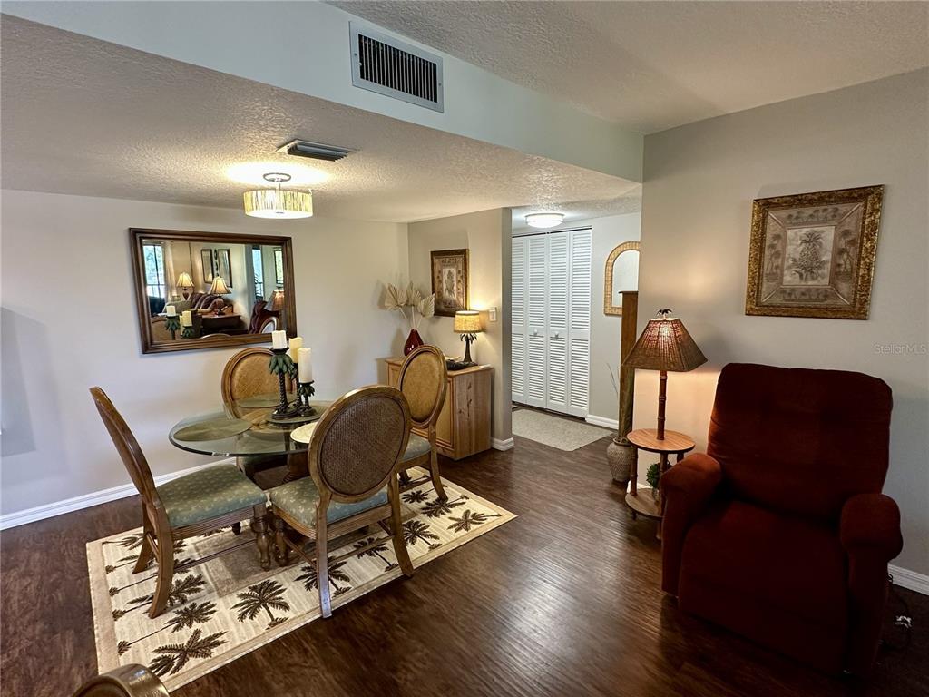 A dining area with a glass table, wicker chairs, and a red recliner on dark flooring — 6116 43RD STREET W UNIT 401D, BRADENTON, FL