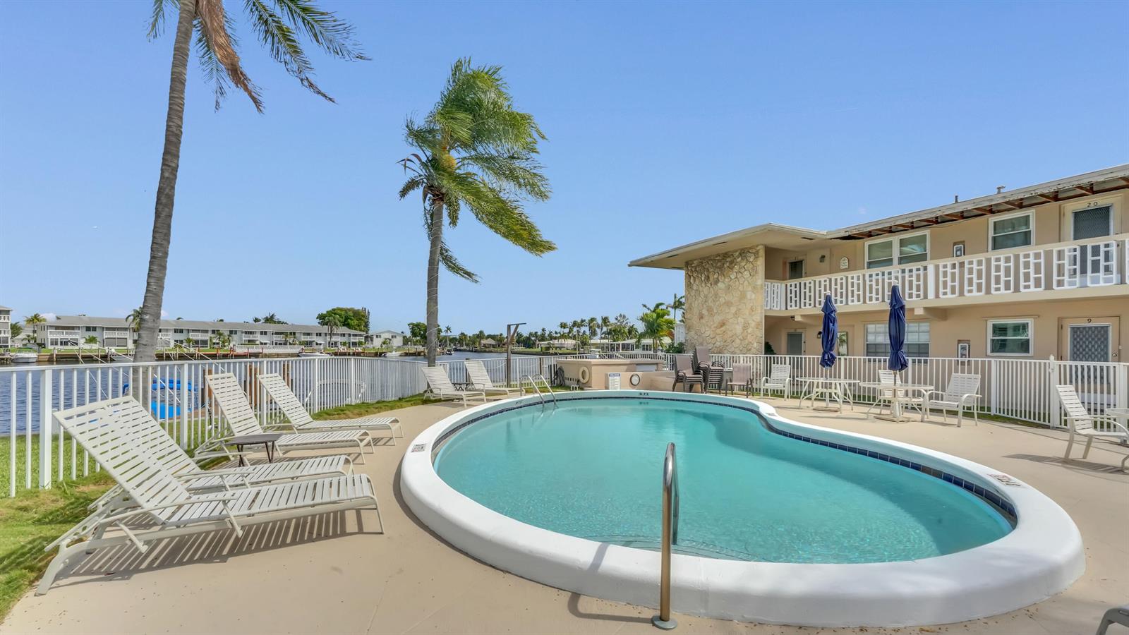 A kidney-shaped swimming pool sits on a patio next to a two-story apartment building — 298 SE 6th Avenue # 2, Pompano Beach FL 33060, POMPANO BEACH, FL