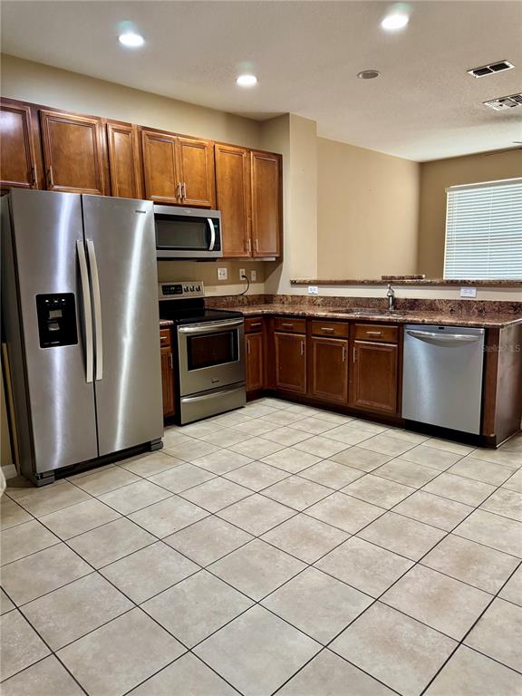A kitchen features wood cabinets, stainless steel appliances, and light-colored tile flooring — 2680 MAYAGUANA STREET, KISSIMMEE, FL