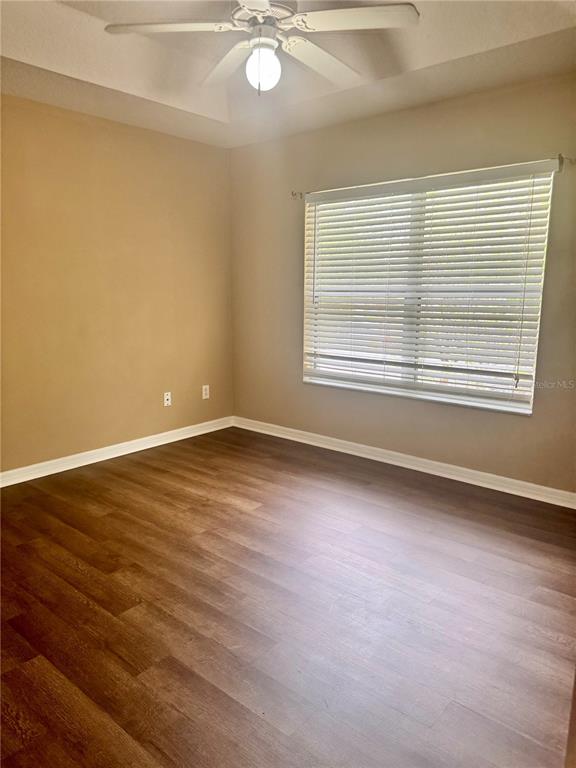 An empty bedroom features wood-look flooring, beige walls, a ceiling fan, and a window with blinds — 2680 MAYAGUANA STREET, KISSIMMEE, FL
