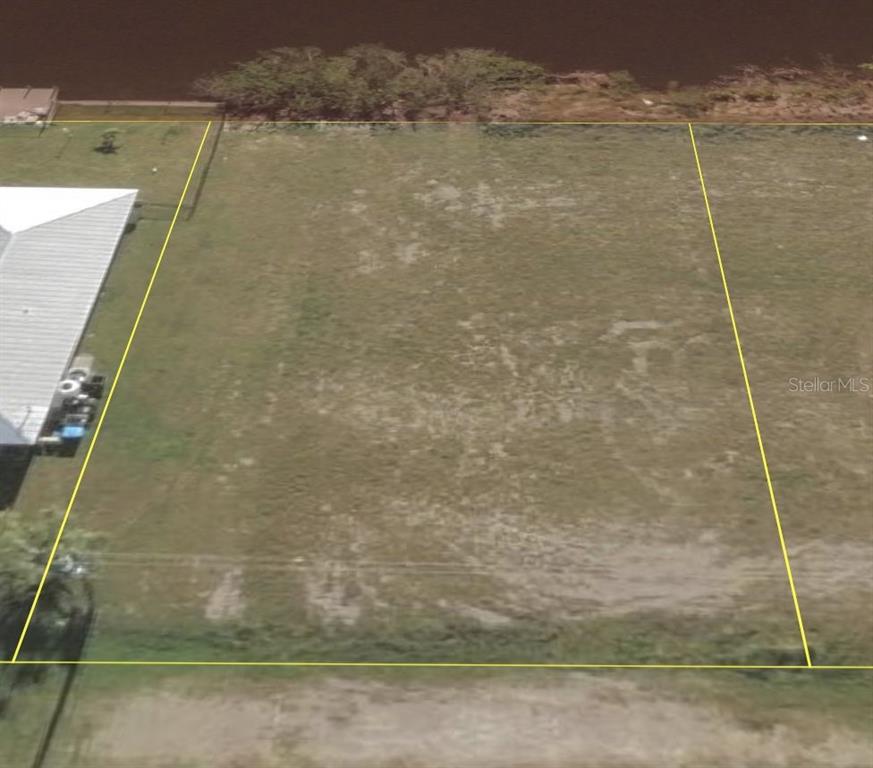 An aerial view shows a vacant, rectangular grassy lot bordering a body of water — 1210 NW 11TH TERRACE, CAPE CORAL, FL