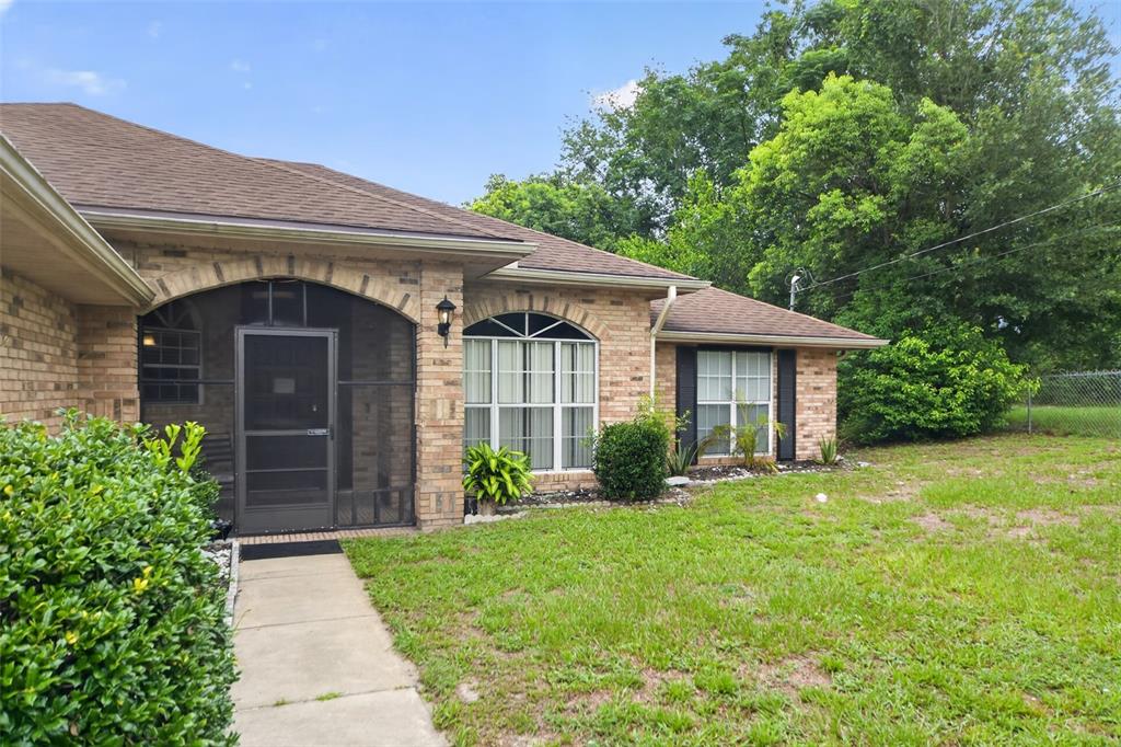 A brick house with a screened-in entryway, arched windows, and a grassy front yard — 1780 W FINLAND DRIVE, DELTONA, FL