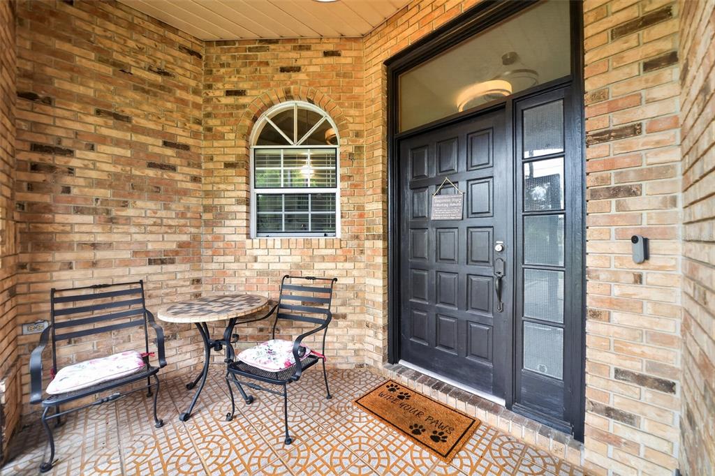 A covered brick porch features a dark front door, a small bistro set, and a doormat — 1780 W FINLAND DRIVE, DELTONA, FL