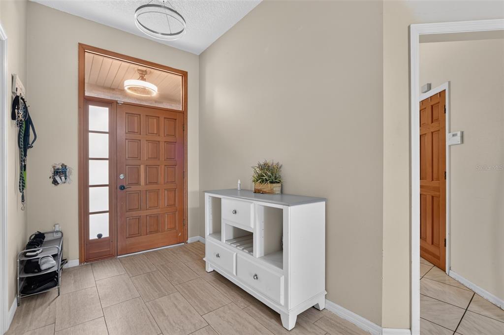 An entryway features a wooden front door, tile flooring, and a white storage console table — 1780 W FINLAND DRIVE, DELTONA, FL