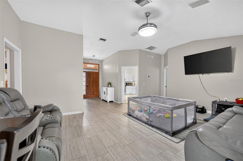 A living room with gray tile floors, a playpen, and a wall-mounted television — 1780 W FINLAND DRIVE, DELTONA, FL