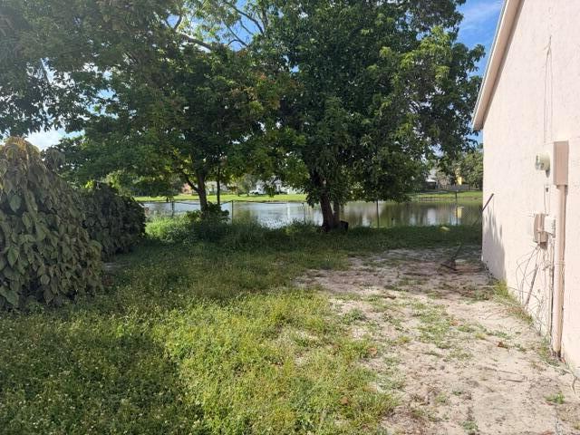 A grassy backyard area with trees and a fence overlooking a small lake — 7355 Pinedale Drive, Boynton Beach FL 33436, BOYNTON BEACH, FL