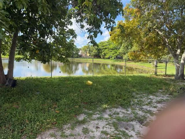 A grassy backyard features a chain-link fence overlooking a small pond with trees — 7355 Pinedale Drive, Boynton Beach FL 33436, BOYNTON BEACH, FL