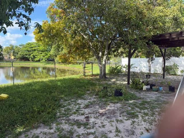 A backyard view featuring a pond, a large tree, and a covered patio area — 7355 Pinedale Drive, Boynton Beach FL 33436, BOYNTON BEACH, FL