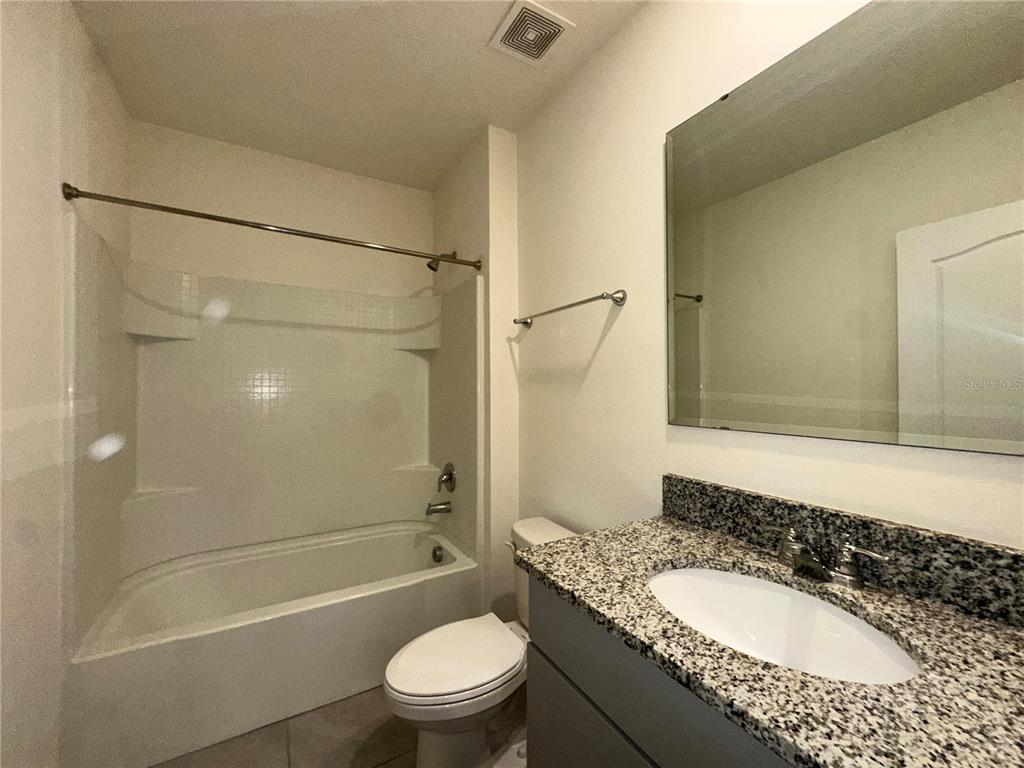 A bathroom features a granite vanity, a toilet, and a shower-tub combination with white walls — 1554 OAK RESERVE DRIVE, KISSIMMEE, FL