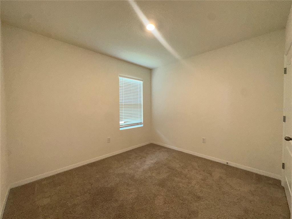 An empty bedroom features beige walls, tan carpeting, and a single window with blinds — 1554 OAK RESERVE DRIVE, KISSIMMEE, FL