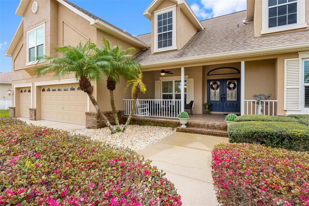 A two-story house features a tan stucco exterior, a front porch, and a landscaped garden — 6224 ROCKROSS AVENUE, NEW PORT RICHEY, FL