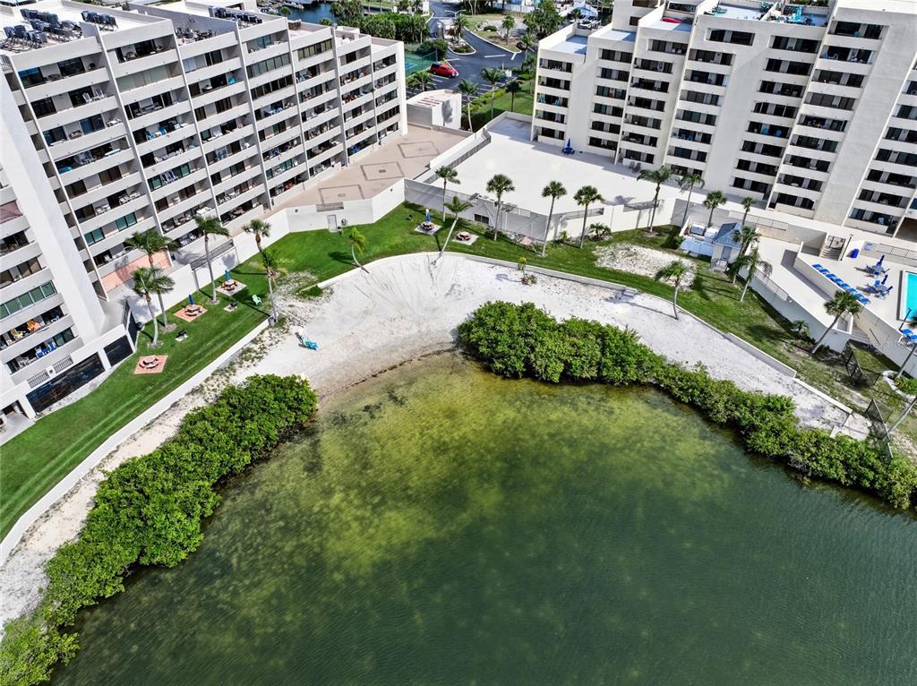An aerial view shows two large apartment buildings flanking a sandy beach and a pond — 6035 SEA RANCH DRIVE UNIT 902, HUDSON, FL