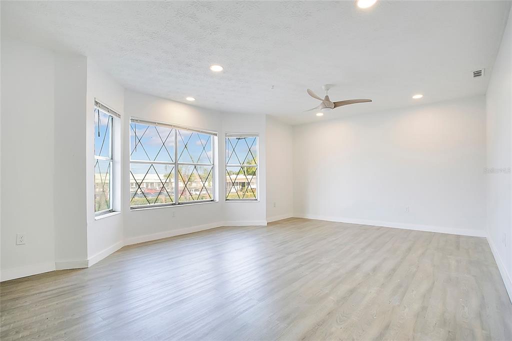 An empty room features light wood-look flooring, white walls, a ceiling fan, and bay windows — 5407 HANSEL AVENUE UNIT G12, ORLANDO, FL