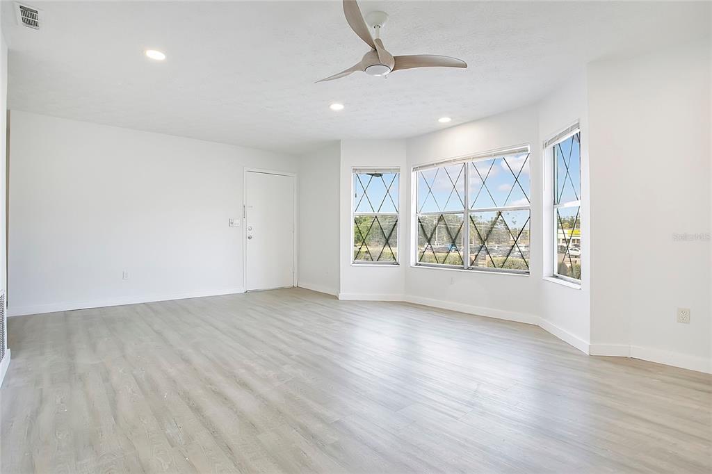 A bright, empty room features light wood-look flooring, white walls, and a large bay window — 5407 HANSEL AVENUE UNIT G12, ORLANDO, FL
