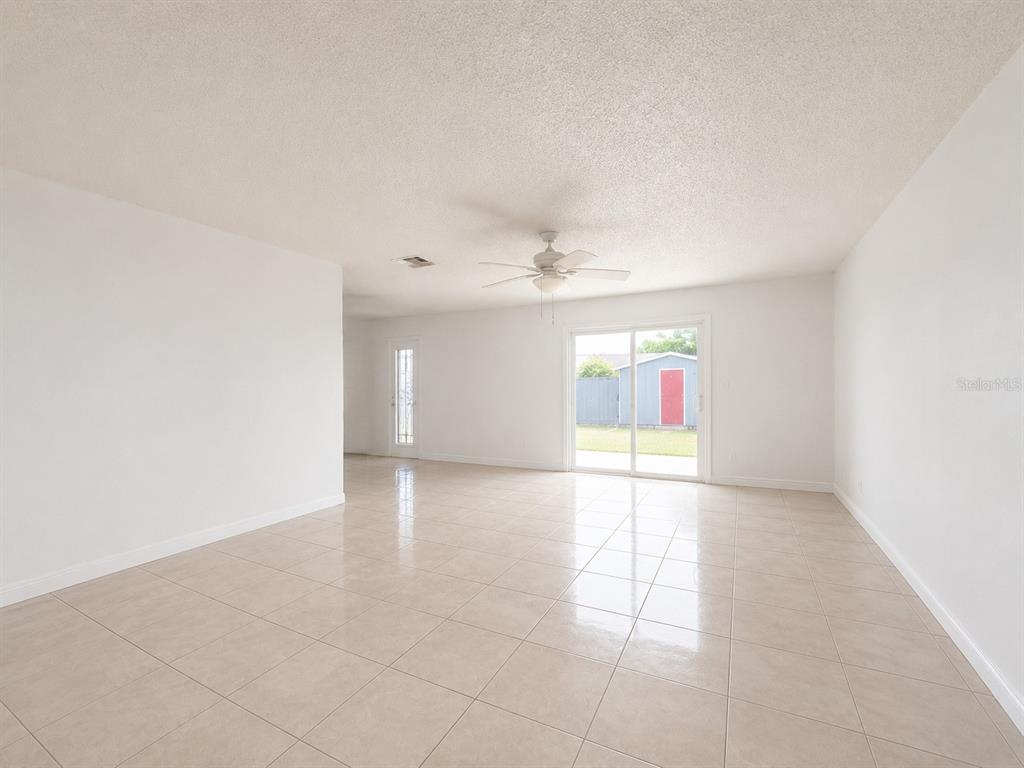 A bright, empty room features white walls, light-colored tile flooring, a ceiling fan, and sliding doors — 5406 ARPANA DRIVE, ORLANDO, FL