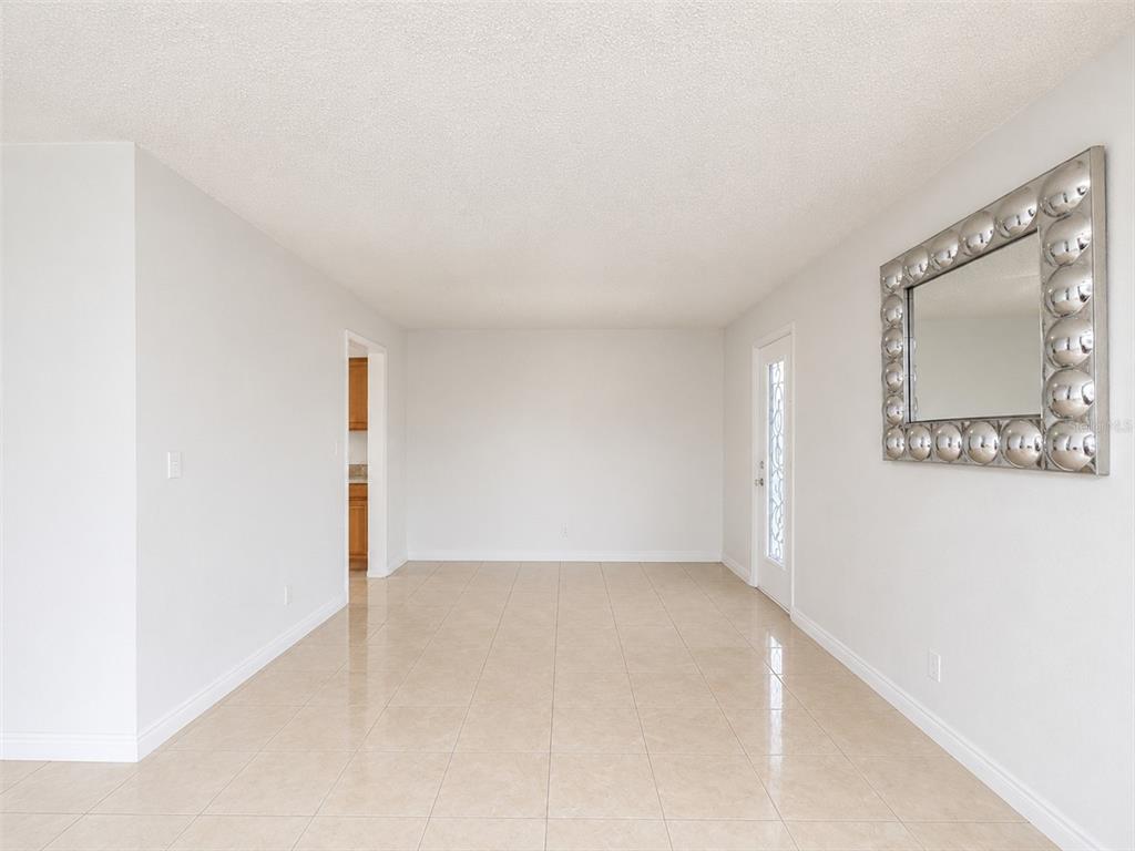 An empty room with light-colored tile flooring, white walls, and a large decorative wall mirror — 5406 ARPANA DRIVE, ORLANDO, FL