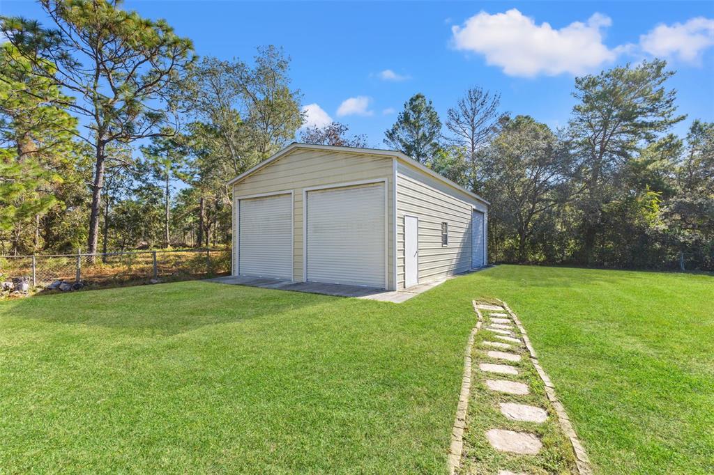 A detached metal garage with two roll-up doors sits on a grassy lawn — 17504 THOMAS BOULEVARD, HUDSON, FL