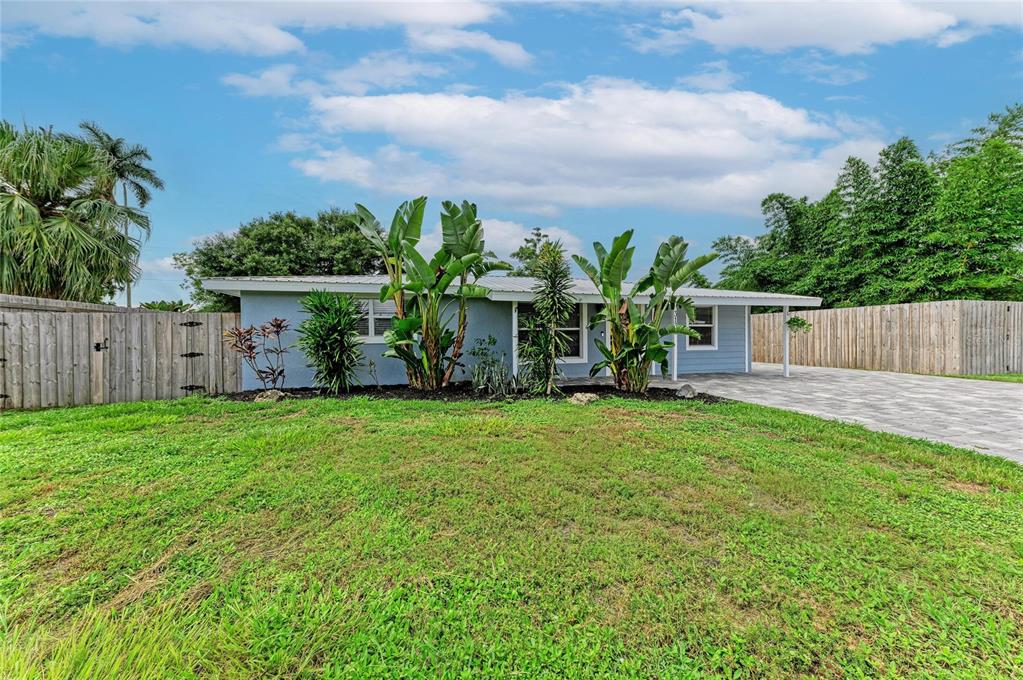 A single-story blue house with a metal roof, tropical landscaping, and a paved driveway — 3138 WILLIAMSBURG STREET, SARASOTA, FL