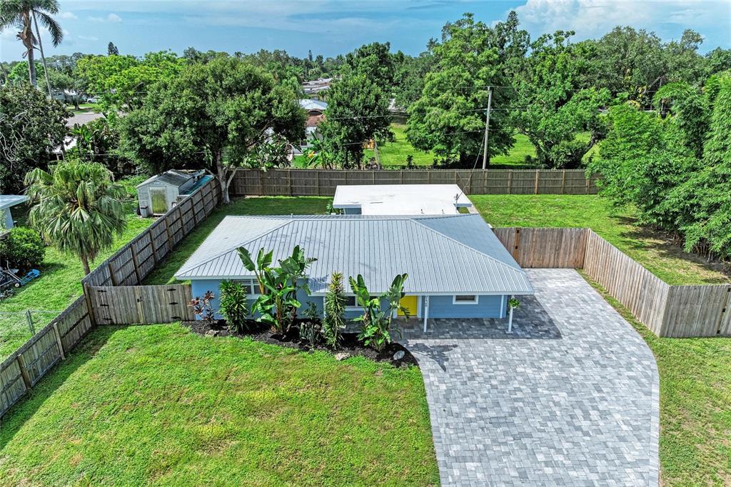 An aerial view shows a blue house with a metal roof, paver driveway, and fenced yard — 3138 WILLIAMSBURG STREET, SARASOTA, FL