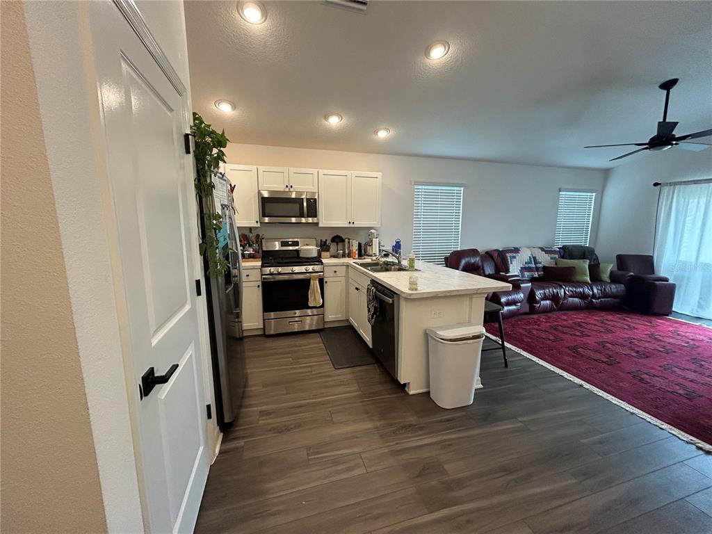 A kitchen with white cabinets and stainless steel appliances opens to a living area — 7328 CATINAZZO COURT, MIDDLETON, FL