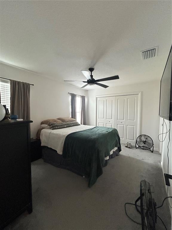 A bedroom features a bed with a green throw, a ceiling fan, and white closet doors — 7328 CATINAZZO COURT, MIDDLETON, FL