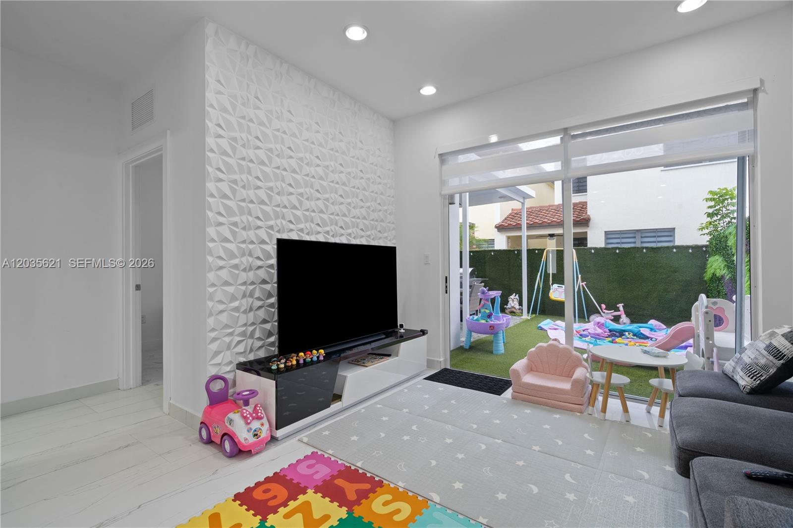 A living room with a textured accent wall, television, and a view of a backyard — 10294 NW 71st Ter, Doral FL 33178, DORAL, FL