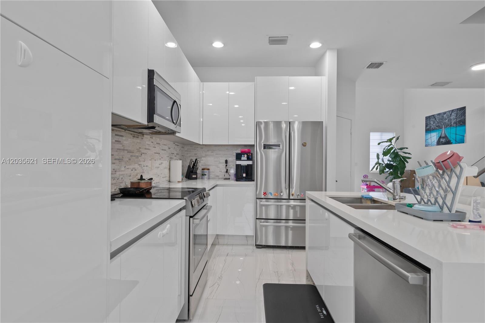 A modern kitchen features white high-gloss cabinets, stainless steel appliances, and white marble-look flooring — 10294 NW 71st Ter, Doral FL 33178, DORAL, FL