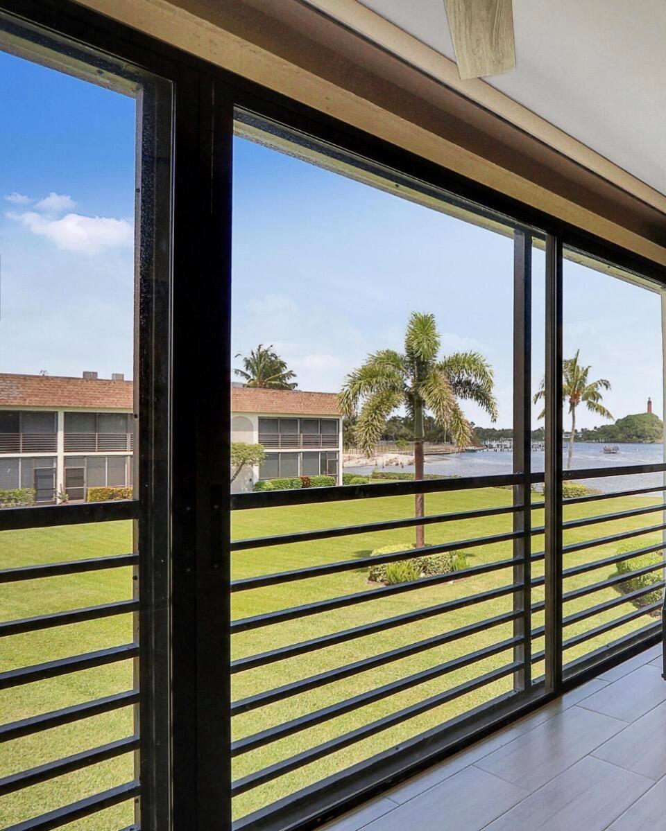 A screened-in balcony with horizontal railings overlooks a grassy lawn, palm trees, and a waterway — 755 Saturn Street # E204, Jupiter FL 33477, JUPITER, FL