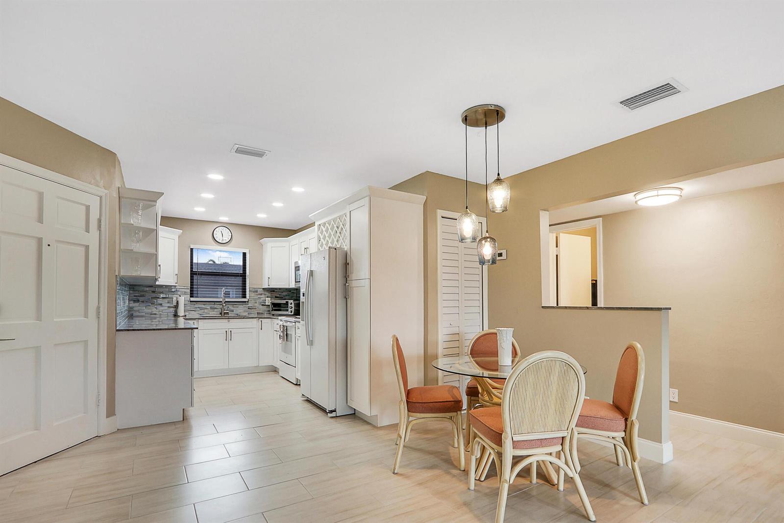 A kitchen with white cabinets and a dining area with a glass table and chairs — 755 Saturn Street # E204, Jupiter FL 33477, JUPITER, FL