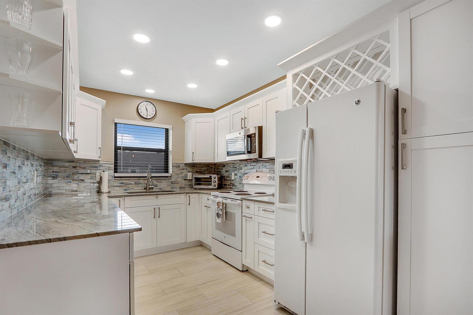 A kitchen features white cabinetry, stainless steel appliances, a tiled backsplash, and granite countertops — 755 Saturn Street # E204, Jupiter FL 33477, JUPITER, FL